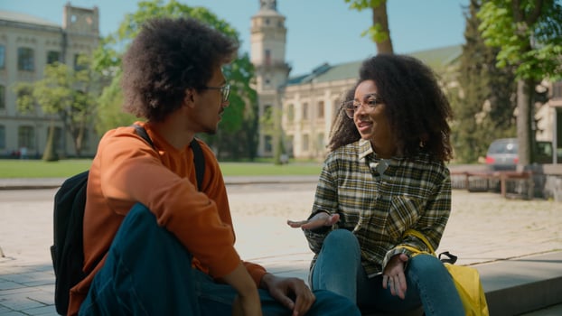 African American ethnic couple students people pupils classmates woman girl lady female man male guy sit outdoors in city talking friendly communicate conversation talk university college high school photo