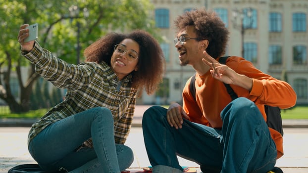 African American ethnic couple students people classmates woman girl female man male guy sit outside in city make selfie photo mobile phone posing camera smartphone picture university college school
