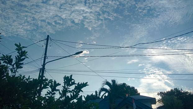 A blue sky with fluffy clouds and a streetlight with power lines. photo