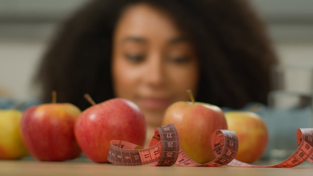 Happy health smiling African American woman ethnic girl female at home kitchen looking enjoying fruits apples glass of water measuring tape at table weight control diet healthy nutrition dieting slim photo
