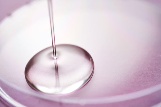 Serum or cosmetic oil flows into a transparent bowl on a purple background. photo