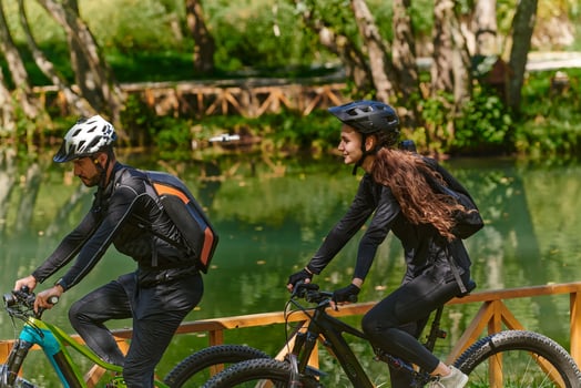 A blissful couple, adorned in professional cycling gear, enjoys a romantic bicycle ride through a park, surrounded by modern natural attractions, radiating love and happiness photo