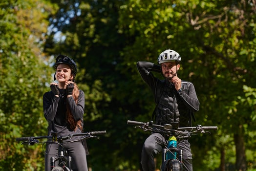 A blissful couple, adorned in professional cycling gear, enjoys a romantic bicycle ride through a park, surrounded by modern natural attractions, radiating love and happiness photo