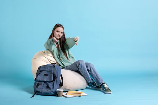 Portrait of upset schoolgirl showing thumbs down sign, disappointed about university exams, studio background. Young girl does disapproving negative hand gesturing regarding homework photo