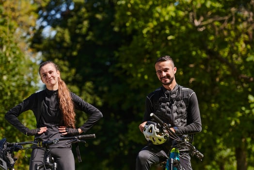 A blissful couple, adorned in professional cycling gear, enjoys a romantic bicycle ride through a park, surrounded by modern natural attractions, radiating love and happiness photo