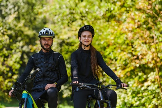 A blissful couple, adorned in professional cycling gear, enjoys a romantic bicycle ride through a park, surrounded by modern natural attractions, radiating love and happiness photo