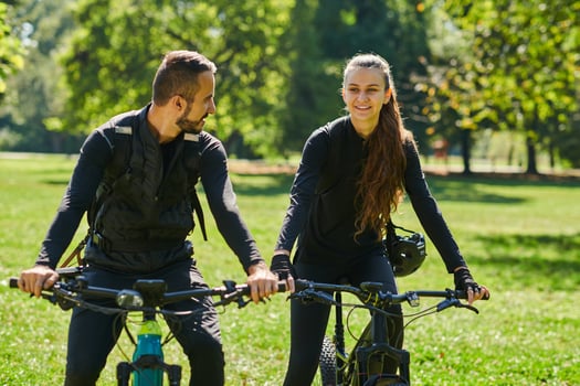A blissful couple, adorned in professional cycling gear, enjoys a romantic bicycle ride through a park, surrounded by modern natural attractions, radiating love and happiness photo