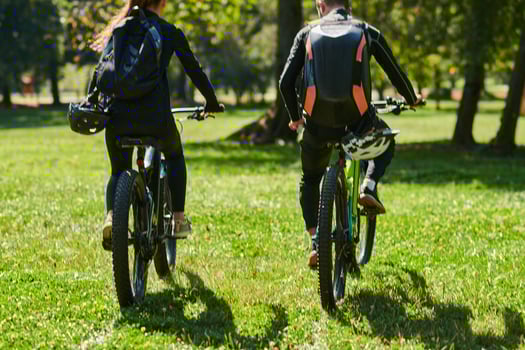A blissful couple, adorned in professional cycling gear, enjoys a romantic bicycle ride through a park, surrounded by modern natural attractions, radiating love and happiness photo