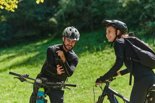 A blissful couple, adorned in professional cycling gear, enjoys a romantic bicycle ride through a park, surrounded by modern natural attractions, radiating love and happiness photo