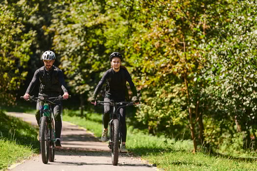 A blissful couple, adorned in professional cycling gear, enjoys a romantic bicycle ride through a park, surrounded by modern natural attractions, radiating love and happiness photo