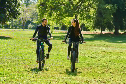 A blissful couple, adorned in professional cycling gear, enjoys a romantic bicycle ride through a park, surrounded by modern natural attractions, radiating love and happiness photo