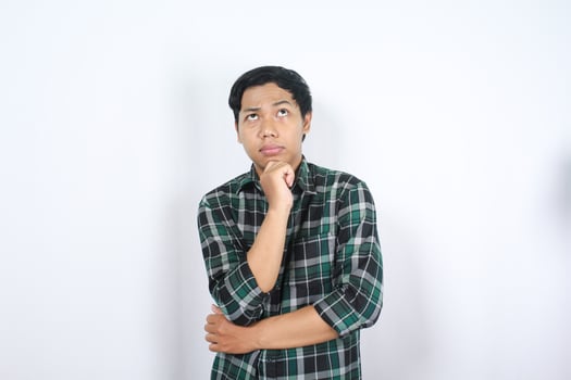 portrait of curious asian young man wearing casual clothes looking above with hand on chin thinking isolated on white background photo