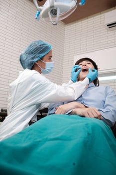 Asian female dentist examine young male patient teeth and toothache stomatology in dental clinic, well-being hygiene checks, and professional orthodontic healthcare work in doctor's office hospital. photo