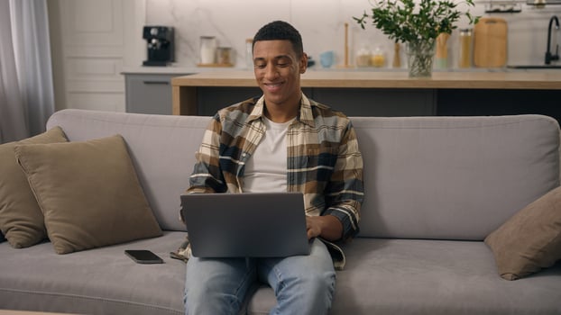 Happy smiling African American ethnic man working at home distant online work studying at sofa guy laptop using computer at couch male using pc playing internet game use app shopping chatting photo
