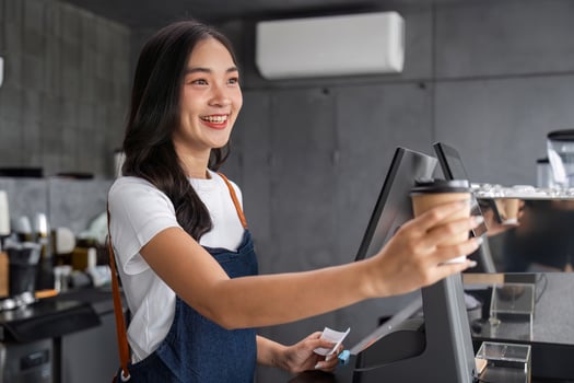 Young Barista Smiling While Making Coffee in a Modern Cafe, Wearing an Apron and Serving a Customer with a Freshly Brewed Cup photo