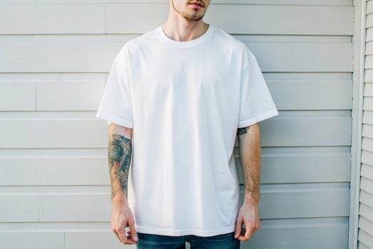 A man with tattoos standing in front of a wall wearing a white t - shirt photo