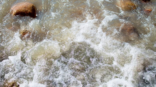 Wild sea, ocean with splashes on stones. Wave rolls onto shore. Top view, drone. Nature photo