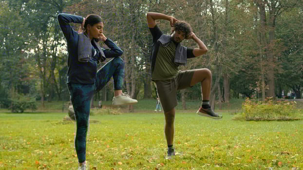 Indian man sportsman athlete instructor personal fitness trainer guy Arabian woman girl sportswoman fit couple sport exercise workout together in park outdoors raise knees to elbows while standing photo