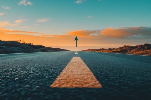 An open asphalt road stretches far and wide into the distance, clearly marked by an arrow, symbolizing a meaningful journey into future achievements and significant growth amidst a stunning sunset photo
