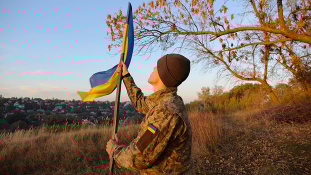 Young man in military uniform waving flag of Ukraine against beautiful sunset at background. Male ukrainian army soldier lifted national banner at countryside. Victory against russian aggression photo