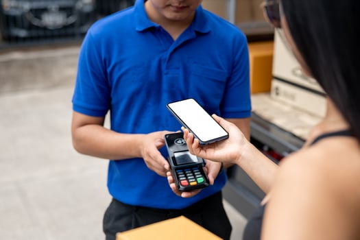 A customer tapping her smartphone on a card reader before receiving a package from a delivery man. photo
