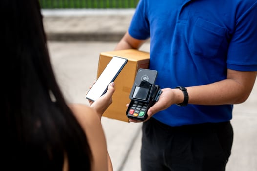 A customer tapping her smartphone on a card reader before receiving a package from a delivery man. photo