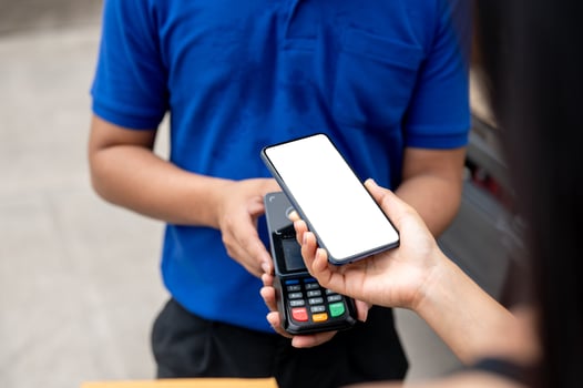 A customer tapping her smartphone on a card reader before receiving a package from a delivery man. photo