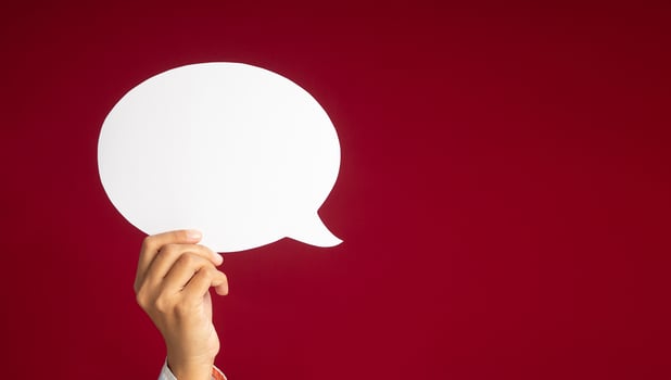 A speech bubble concept. Hand holding an empty white speech bubble over on a red background with copy space for text. Close-up photo