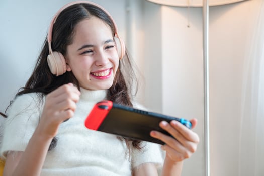 Portrait of cheerful young girl play game in living room, Teenage girl in headphones having fun playing with portable gaming console photo