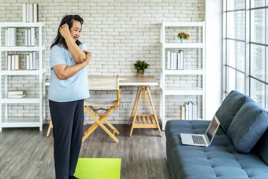 Elderly asian woman watching tutorial doing stretching fitness exercise yoga. Elderly women training online courses on laptop while exercising in living room. Workout training online concept photo