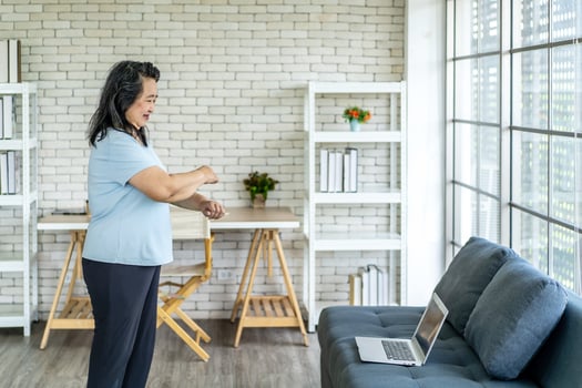Elderly asian woman watching tutorial doing stretching fitness exercise yoga. Elderly women training online courses on laptop while exercising in living room. Workout training online concept photo