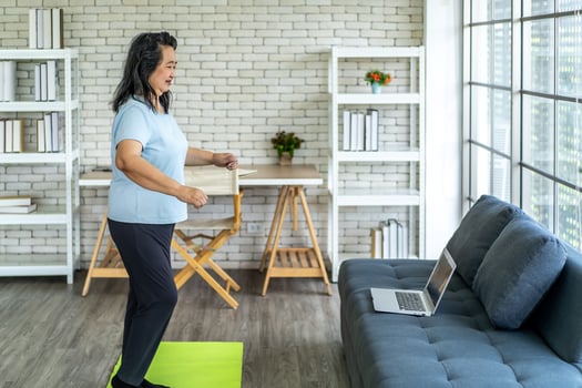 Elderly asian woman watching tutorial doing stretching fitness exercise yoga. Elderly women training online courses on laptop while exercising in living room. Workout training online concept photo