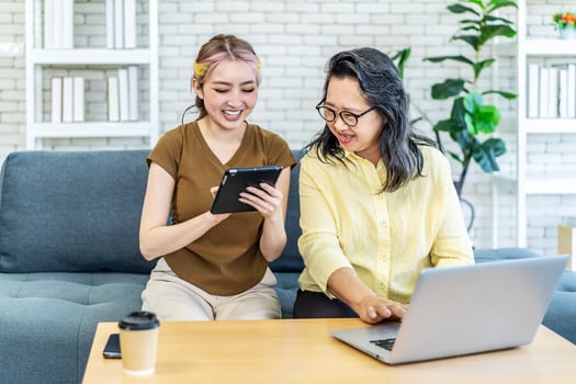 Happy asian senior mother and young woman daughter shopping online with laptop computer and tablet at home. Asian family making purchases online, Buying ordering products on the internet. photo
