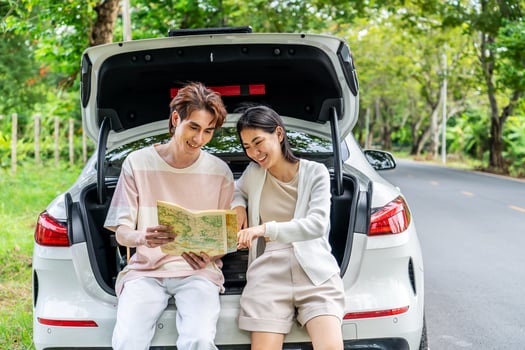 Traveler couple on road trip, man and woman sitting together in car trunk using map on journey during the trip, Two young boy and girl travel, Two friend traveling on vacation, searching road in map photo