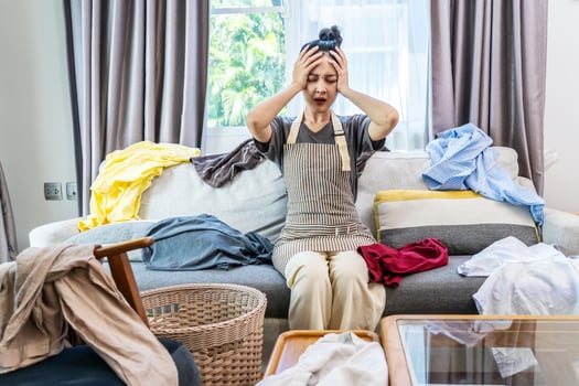 Stressed young woman asian sitting on the sofa in the living room and among a mess at home, woman sitting among scattered clothes on sofa and ignoring, woman frowning and letting out soft sigh. photo