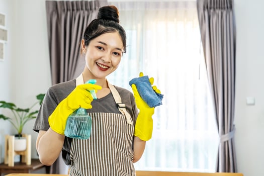 Happy young housewife mistress female in yellow protective rubber gloves with spray and rag,cleaning house, enjoying housework, Asian maid committed to maintaining the highest standards of cleanliness photo