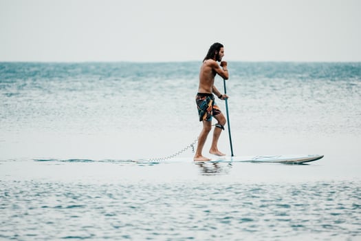 Sea man sup. Asian athlete man swimming in sea and paddleboarding at summer sunset. Healthy strong male enjoy outdoor active lifestyle and water sports on holiday vacation. photo