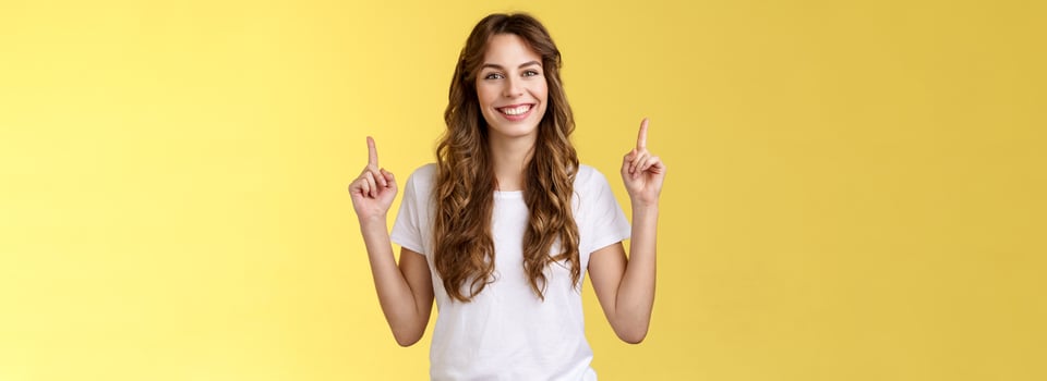 Self-assured confident lively charming european tall girl showing advicing cool promo pointing up index fingers smiling toothy delighted introuce excellent choice advertisement yellow background photo