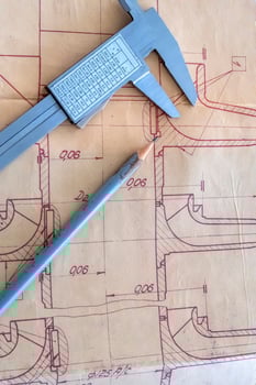 A caliper and pencil over industrial plan. A photo closeup.