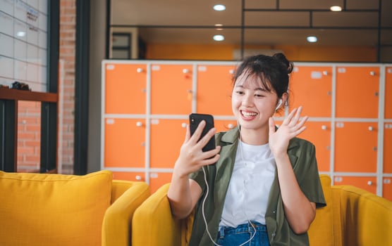 Smiling young asian woman using mobile phone checking social media,app playing game, shopping online, ordering delivery relax while sitting on a couch at cafe with laptop computer photo