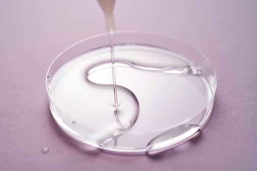 Serum or cosmetic oil flows into a transparent bowl on a purple background. photo
