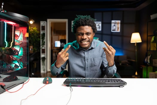 Brass gamer at computer desktop insulting rival players while playing competitive multiplayer videogames. Cheeky man throwing middle fingers gesturing at opponents in internet esports game photo