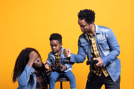 Enthusiastic father playing online games with his baby boy using controller, both parents enjoying leisure time with their small kid. African american happy family play with a joystick. photo