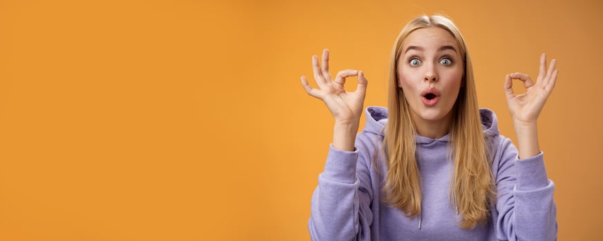 Amused talented creative young blond female tell excellent idea show okay no problem gesture persuade friends everything alright standing excited orange background ok signs, folding lips amazed photo