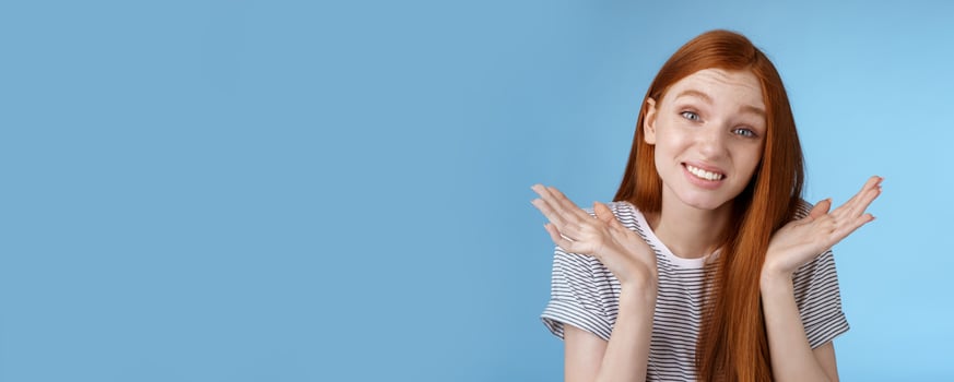 Awkward apologizing cute redhead girlfriend say sorry shrugging spread hands sideways puzzled smiling uncomfortably standing clueless unaware forgetting meeting, posing blue background photo
