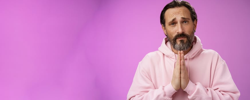 Upset handsome bearded mature man need help asking forgiveness supplicating press palms together praying frowning sorrow begging favour lend money, standing purple background miserable photo