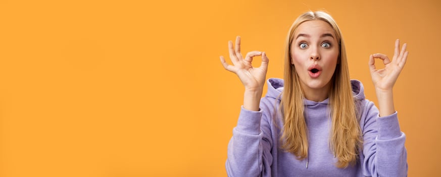 Amused talented creative young blond female tell excellent idea show okay no problem gesture persuade friends everything alright standing excited orange background ok signs, folding lips amazed photo