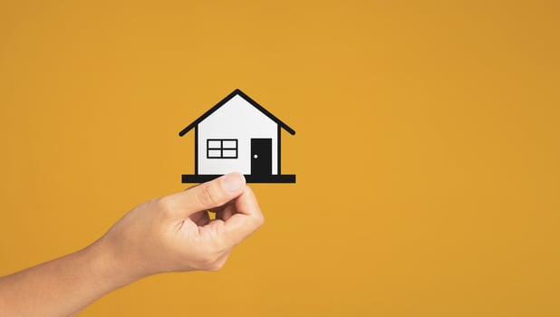 Business and real estate concept. Close-up of hand holding a mini paper house while standing on a yellow background in the studio. Space for text. Property insurance and security photo
