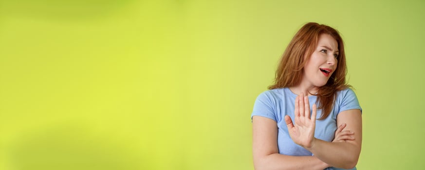 Enough wasting my time. Ignorant uninterested redhead mature woman turn away displeased reluctant show stop no gesture hold palm refusal rejecting unpleasant offer green background photo