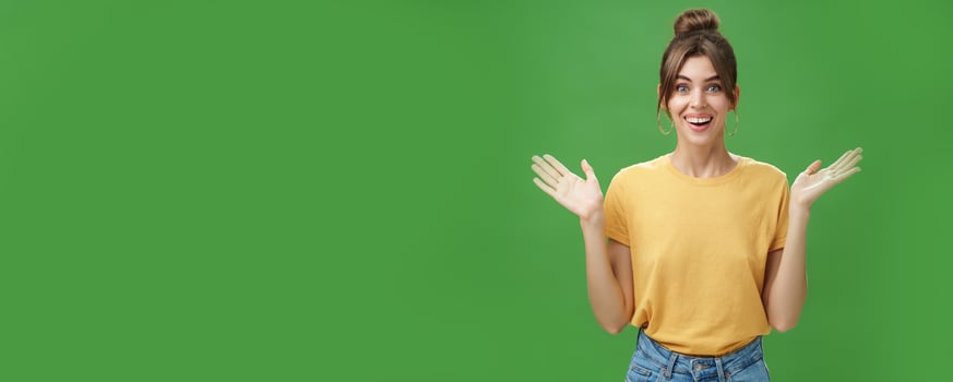 Amazed and surprised woman reacting to astonishing gift raising hands near shoulders smiling happily at camera being delighted and pleased with awesome surprise made by friends over green wall photo